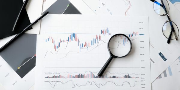 An image of research papers on a busy desk, a magnifying glass and a pair of glass sit on top.